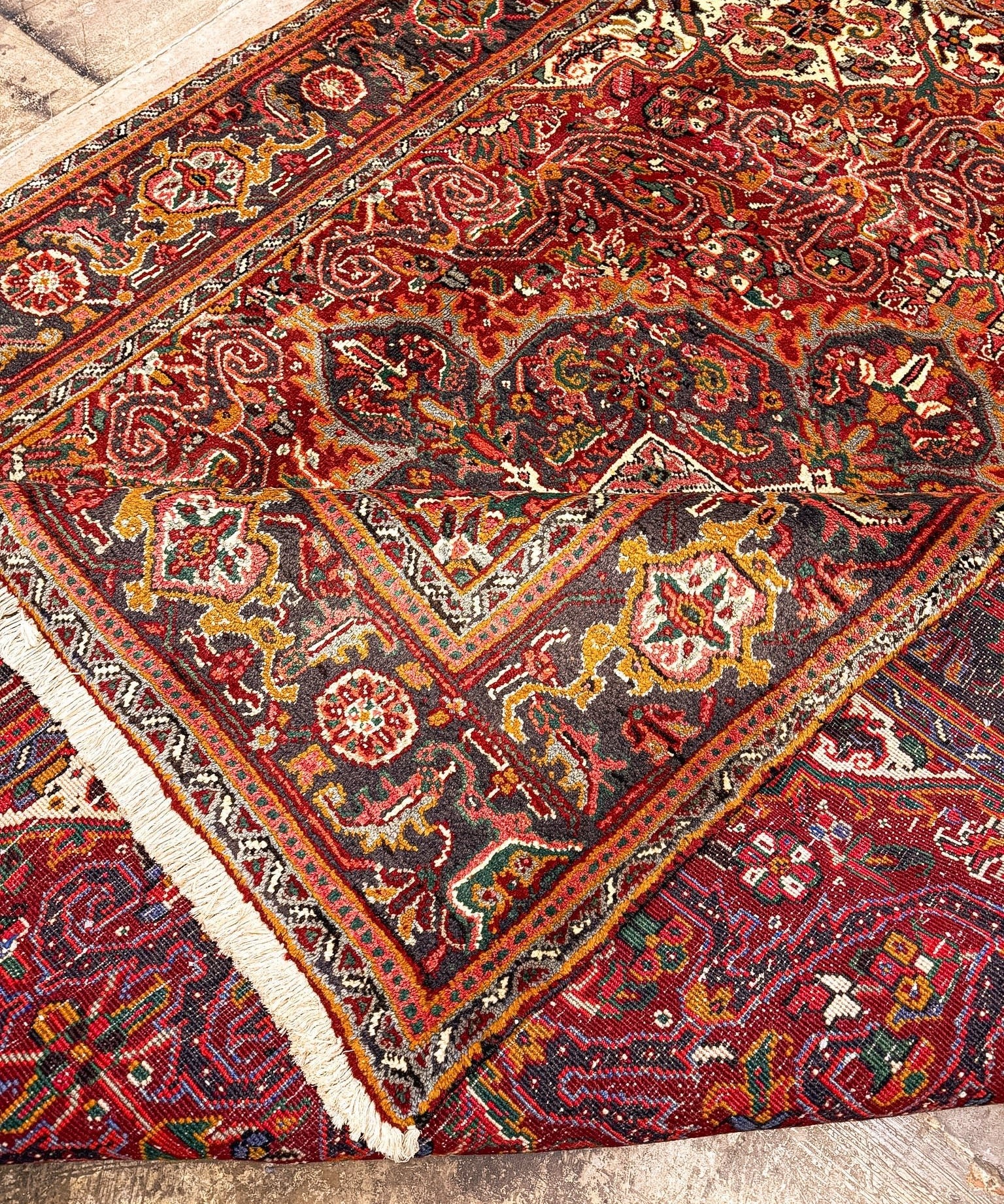 Heriz rug corner detail with red medallions, navy accents, cream border fringe