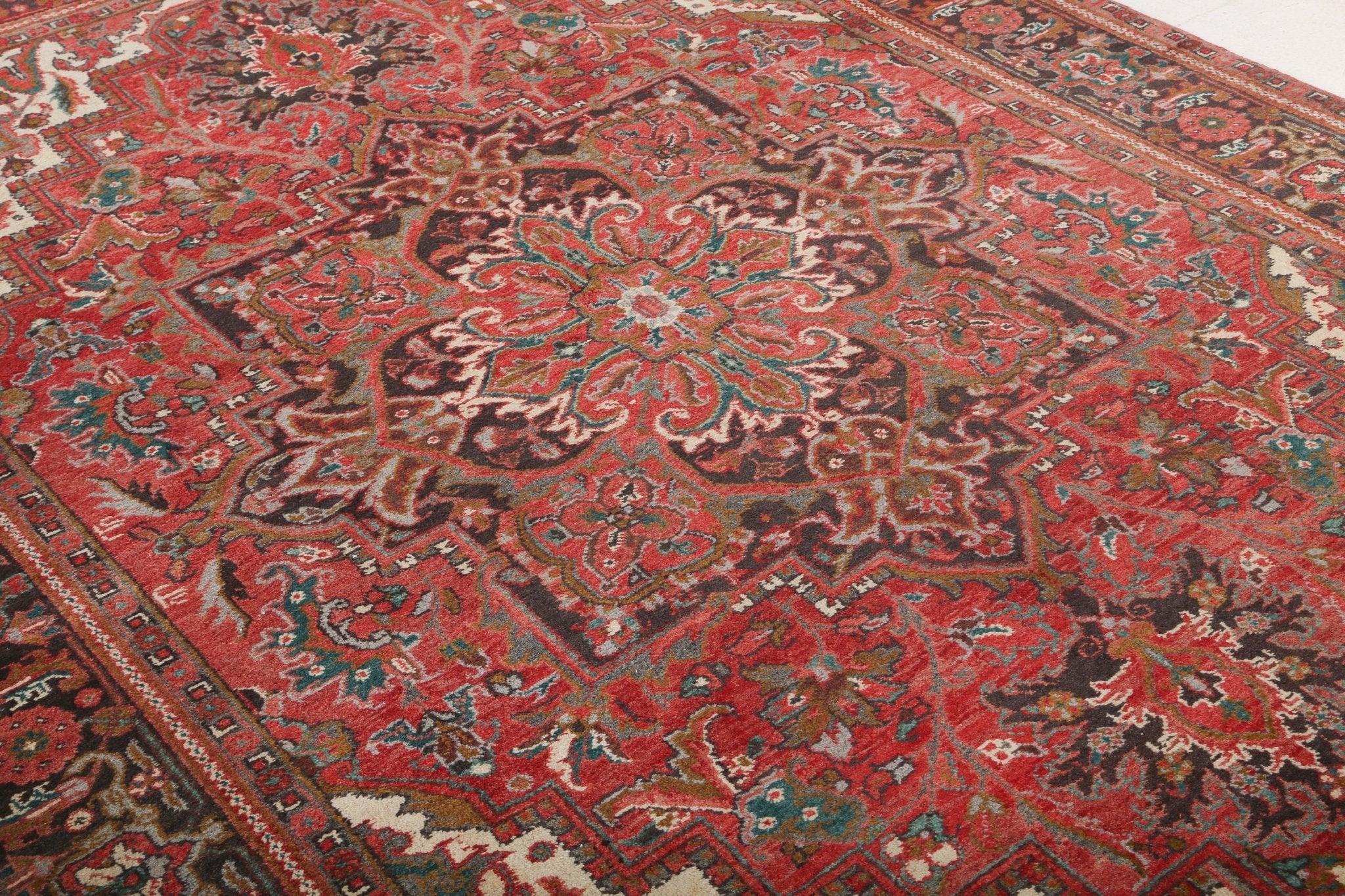 Persian Heriz style area rug with red field, teal accents, and detailed corner motifs