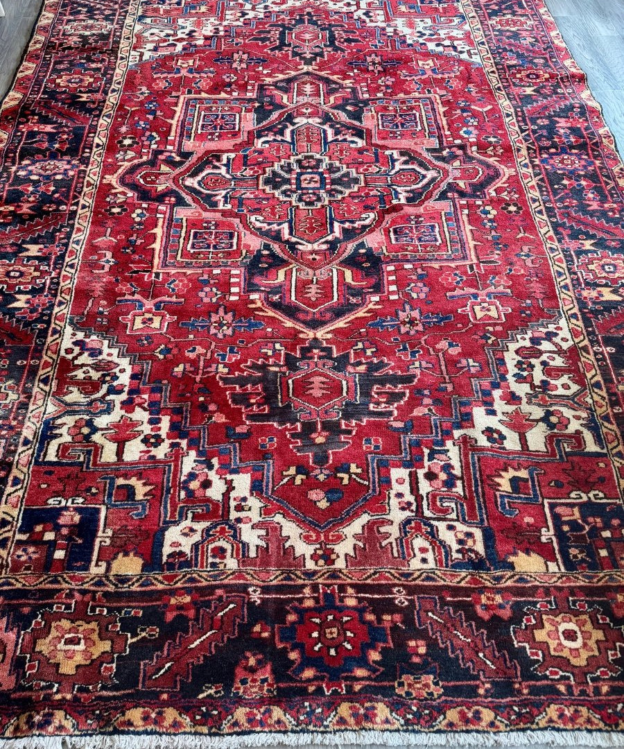 Persian Heriz rug laid flat with red central medallions and navy border stripes.