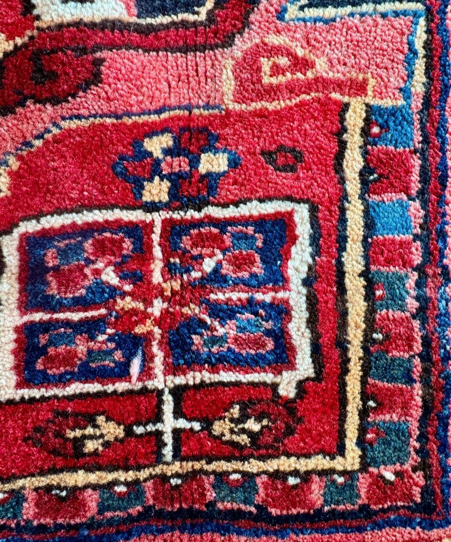 Persian Heriz rug rug detail with red and navy panels, beige framing, and inset corner motifs.