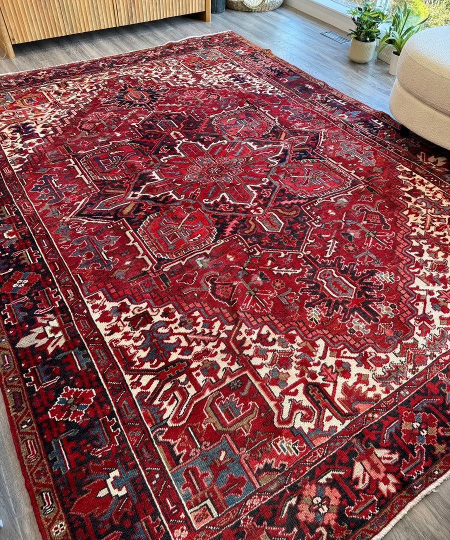 Red Persian Heriz-style rug with cream and navy pattern, laid flat on the floor