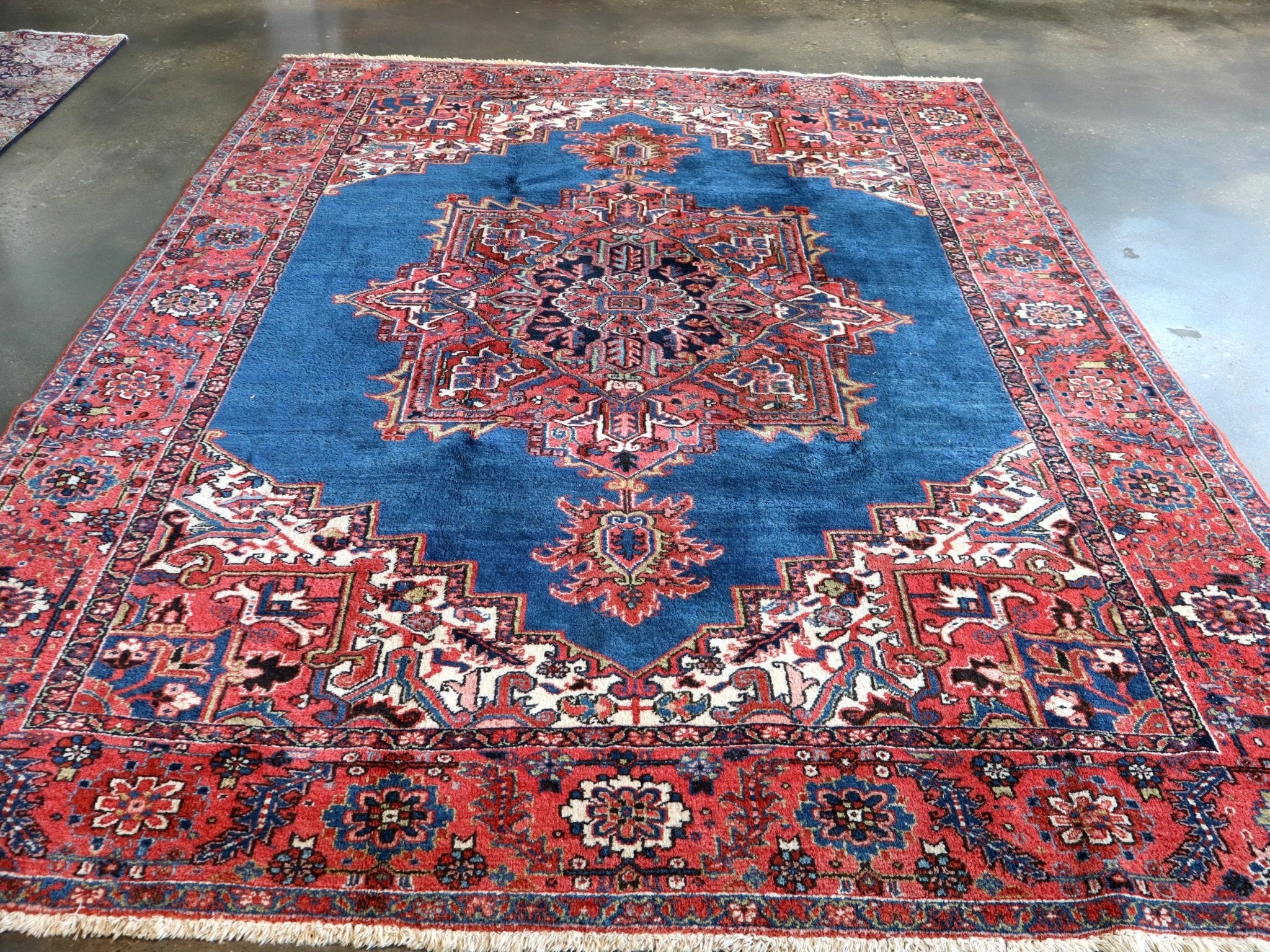 Persian Heriz rug featuring blue field, red border, and symmetrical central design