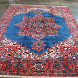 Persian Heriz rug featuring blue field, red border, and symmetrical central design