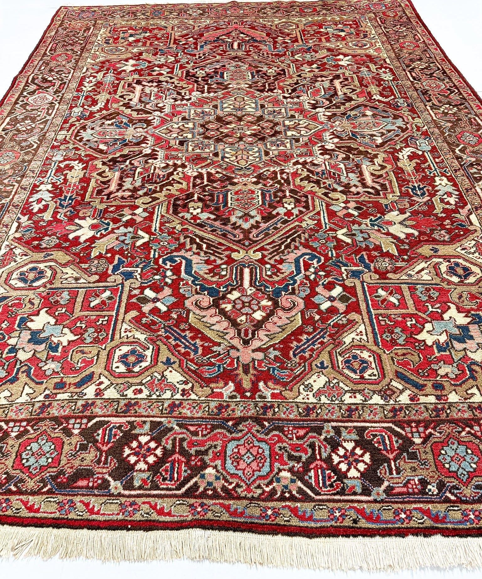 Heriz rug full view with red center medallion, colorful motifs, and light cream fringed ends