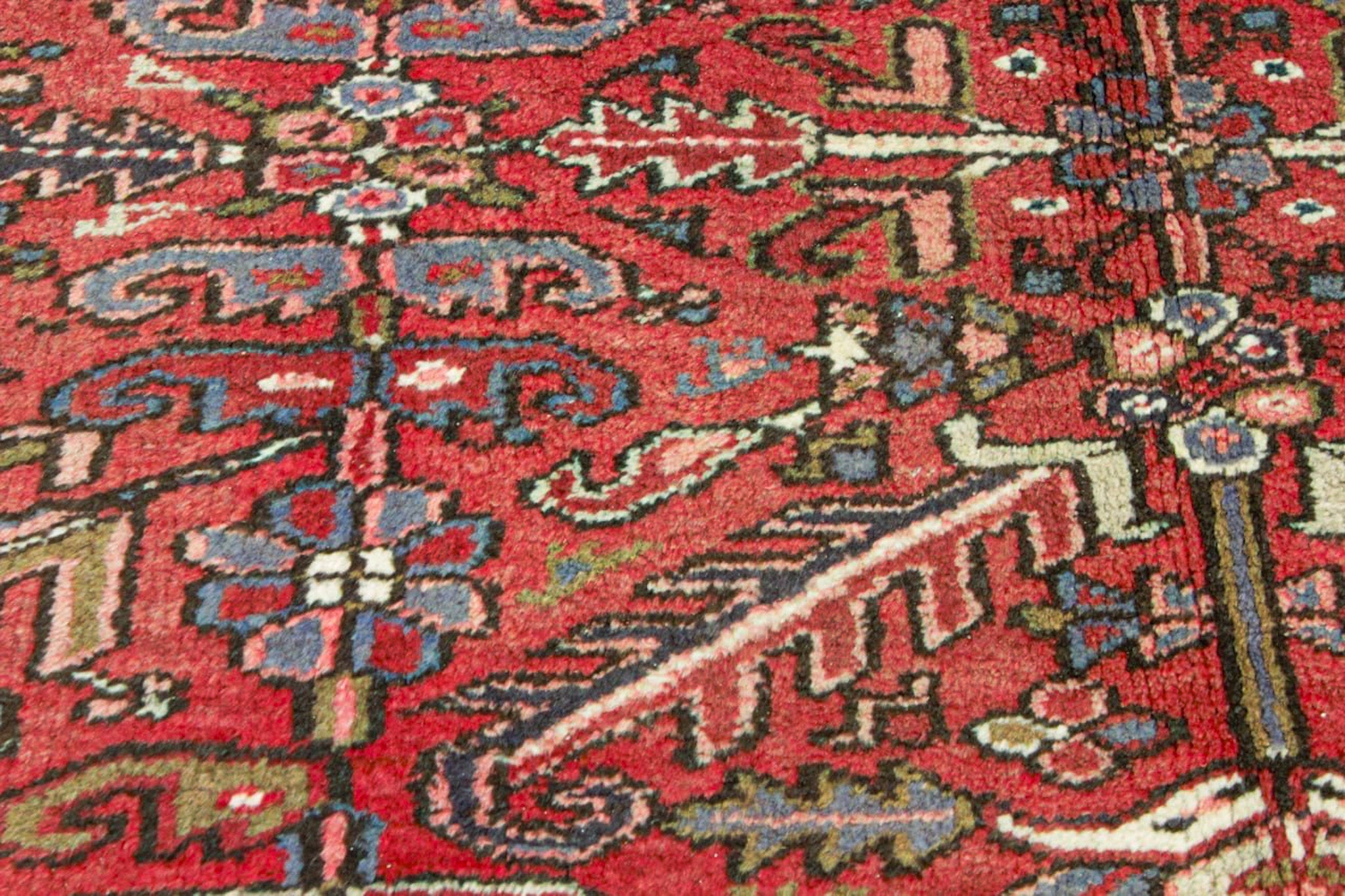 Red rug close-up with dense floral and geometric motifs in cream, blue, and dark tones