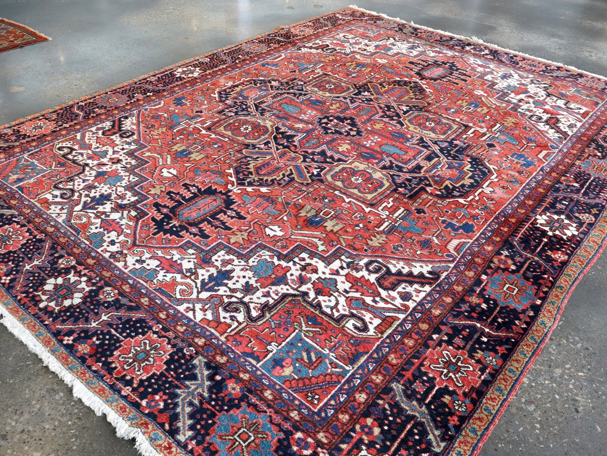 Persian Heriz rug in three-quarter view with red and navy geometric pattern and fringe