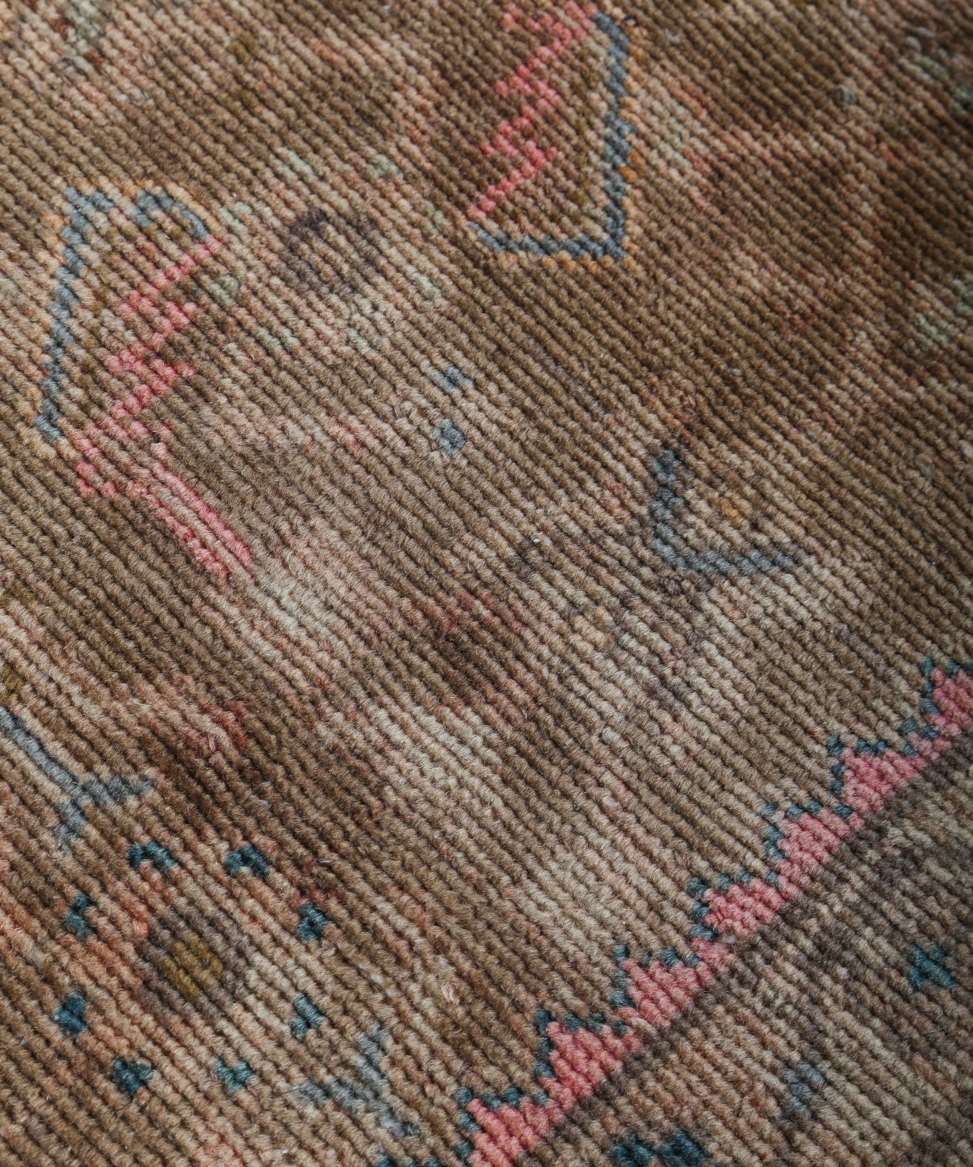 Close-up of tan Persian rug with blue and pink geometric figures and texture.
