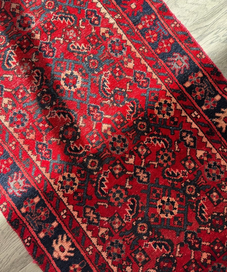 Close-up Persian-style runner rug corner with red, navy, and beige geometric motifs
