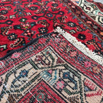 Corner close-up of red runner rug showing ivory fringe and detailed motifs.