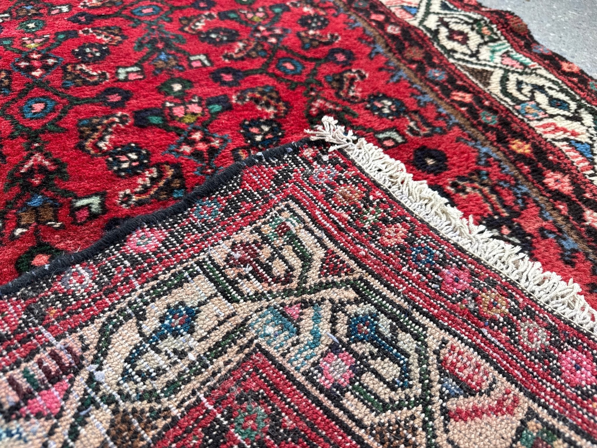 Corner close-up of red runner rug showing ivory fringe and detailed motifs.