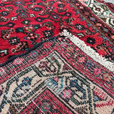 Corner close-up of red runner rug showing ivory fringe and detailed motifs.