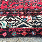 Lower section close-up of red runner rug with repeating medallion and stripe border.