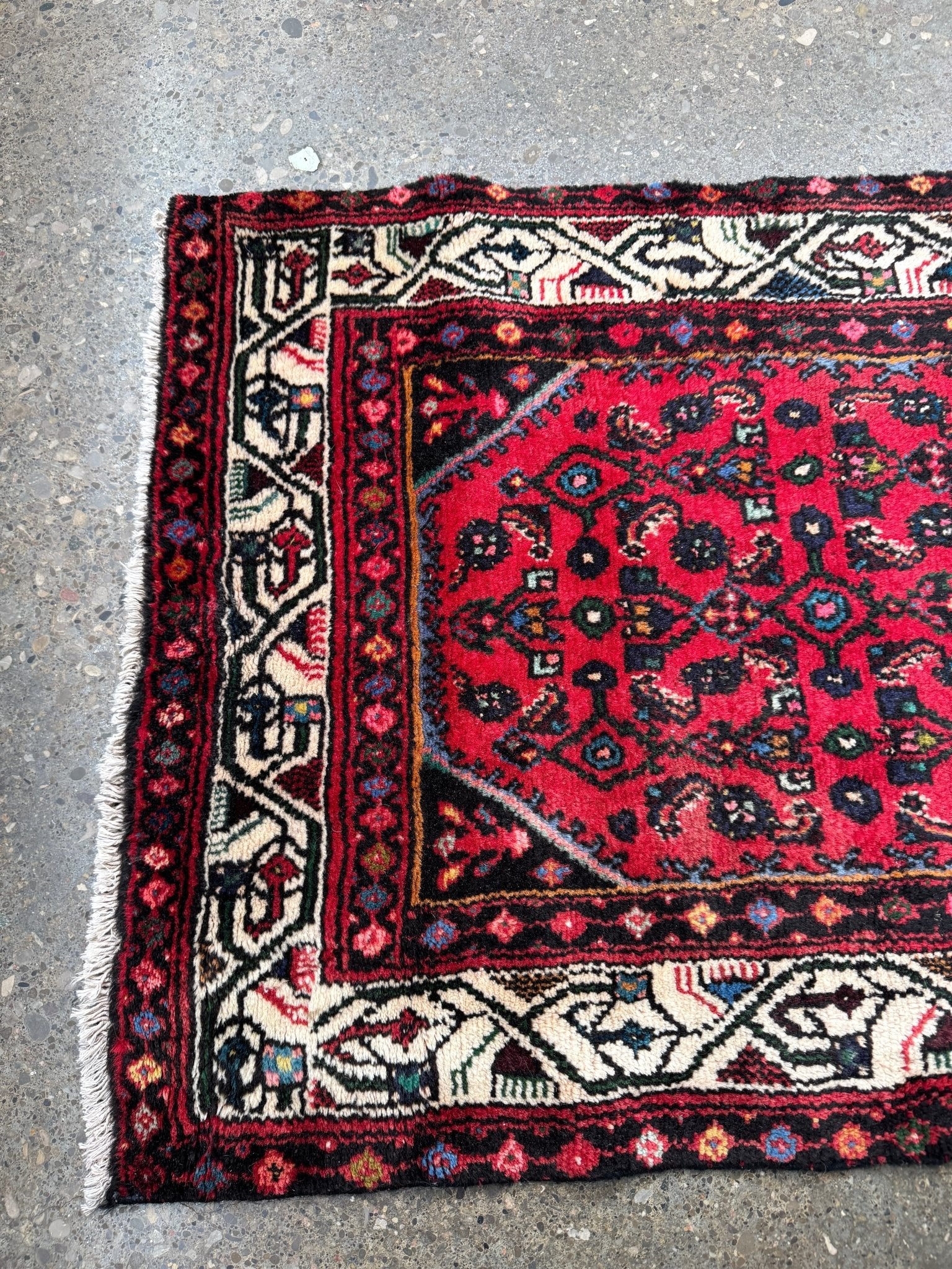 Persian runner rug, folded corner view with red center and cream border stripes