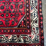 Edge close-up of red runner rug with cream patterned border and fringe tassels.