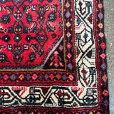 Edge close-up of red runner rug with cream patterned border and fringe tassels.