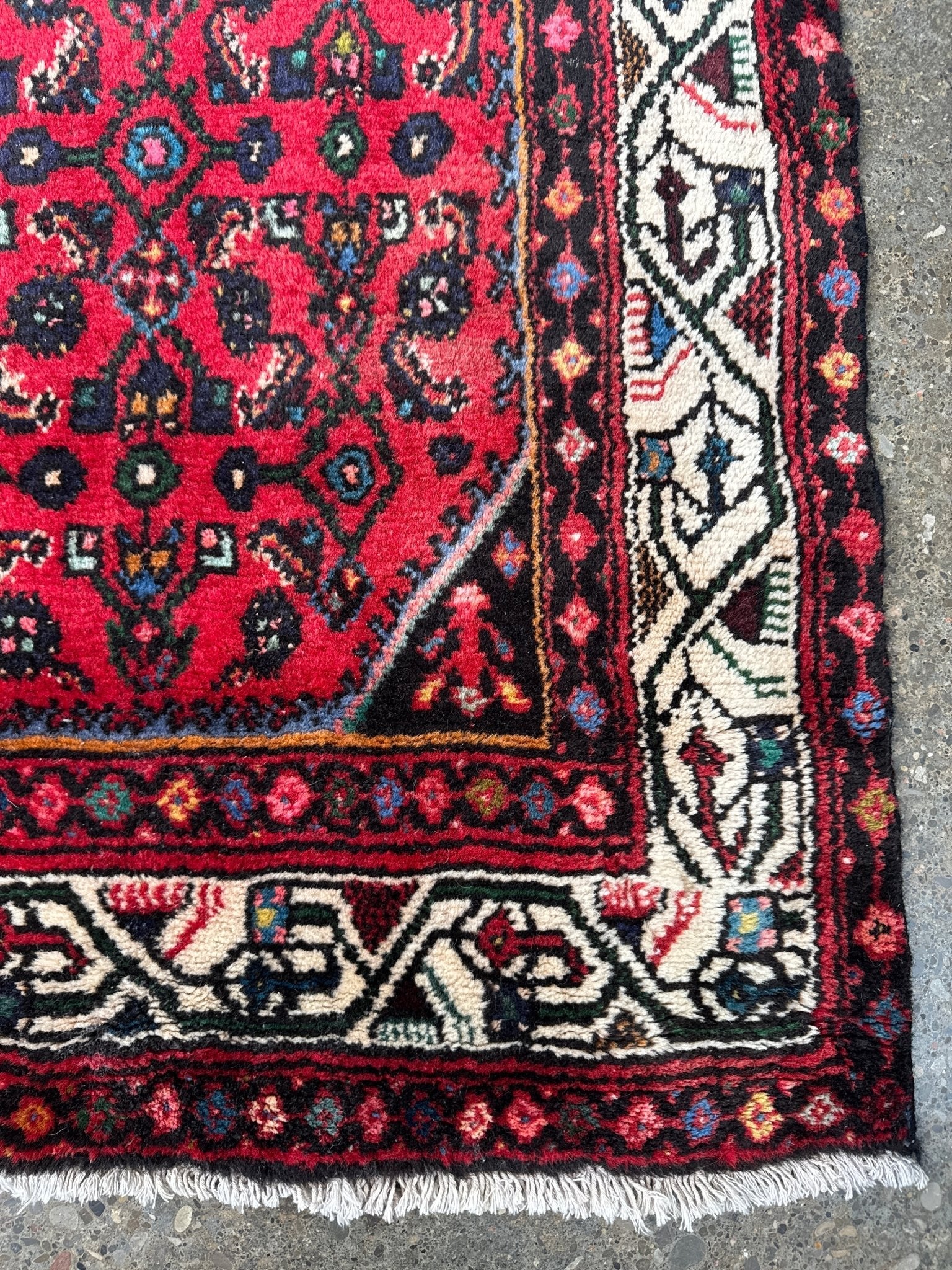 Edge close-up of red runner rug with cream patterned border and fringe tassels.