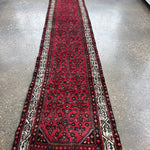 Long red patterned runner rug with cream, navy, and green border details.