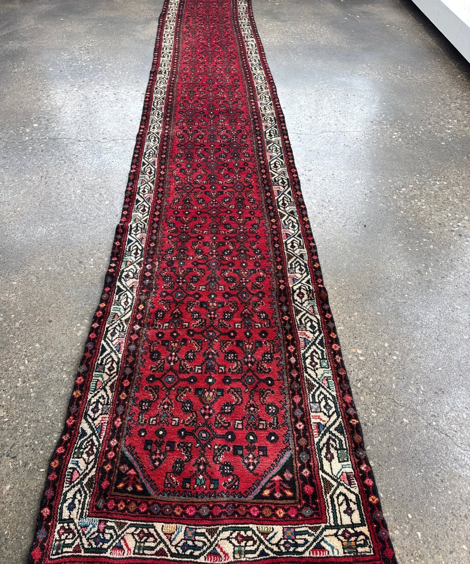 Long red patterned runner rug with cream, navy, and green border details.