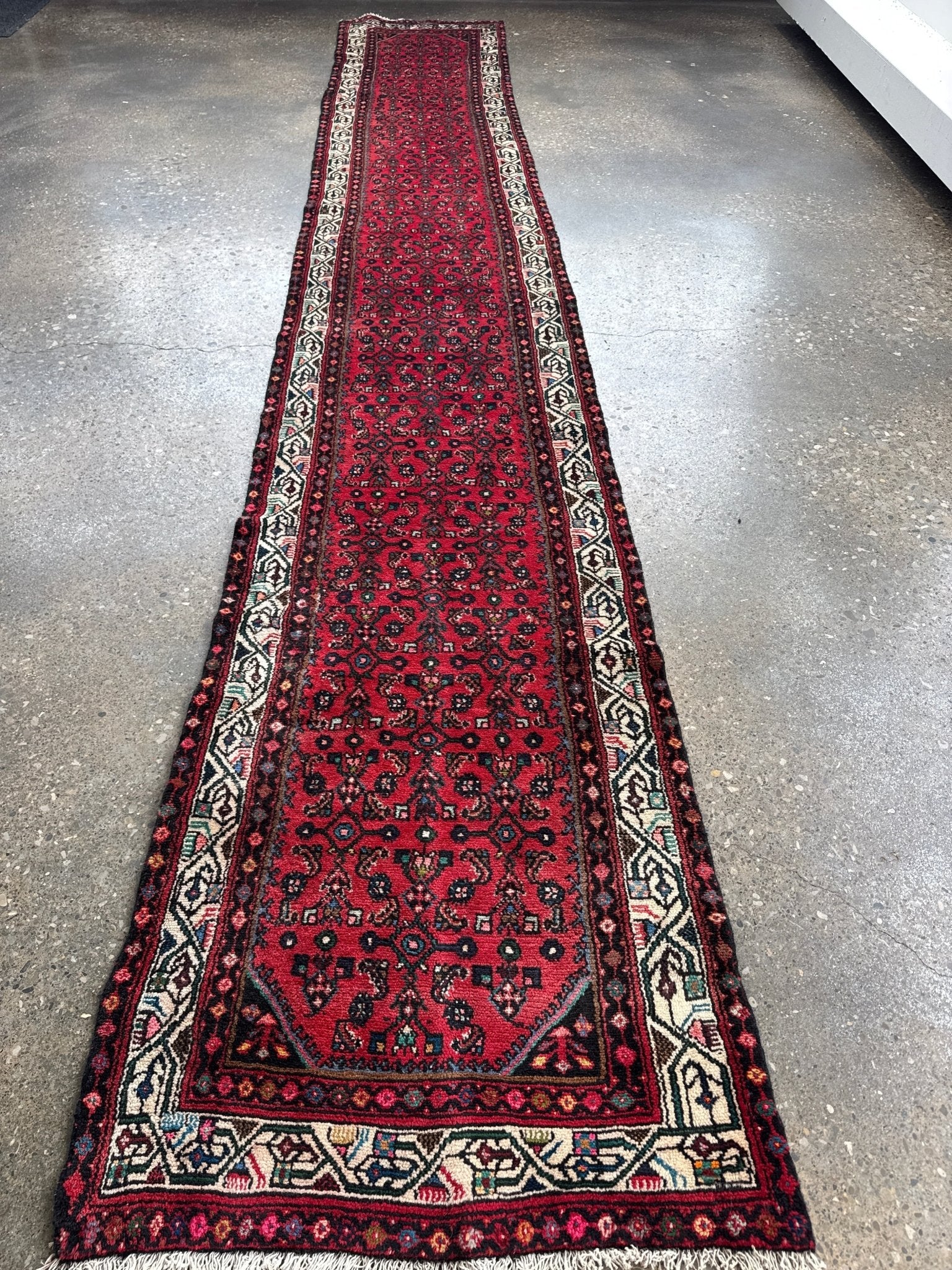 Long red patterned runner rug with cream, navy, and green border details.