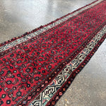 Red runner rug corner view with ornate navy and cream motifs along the edge.