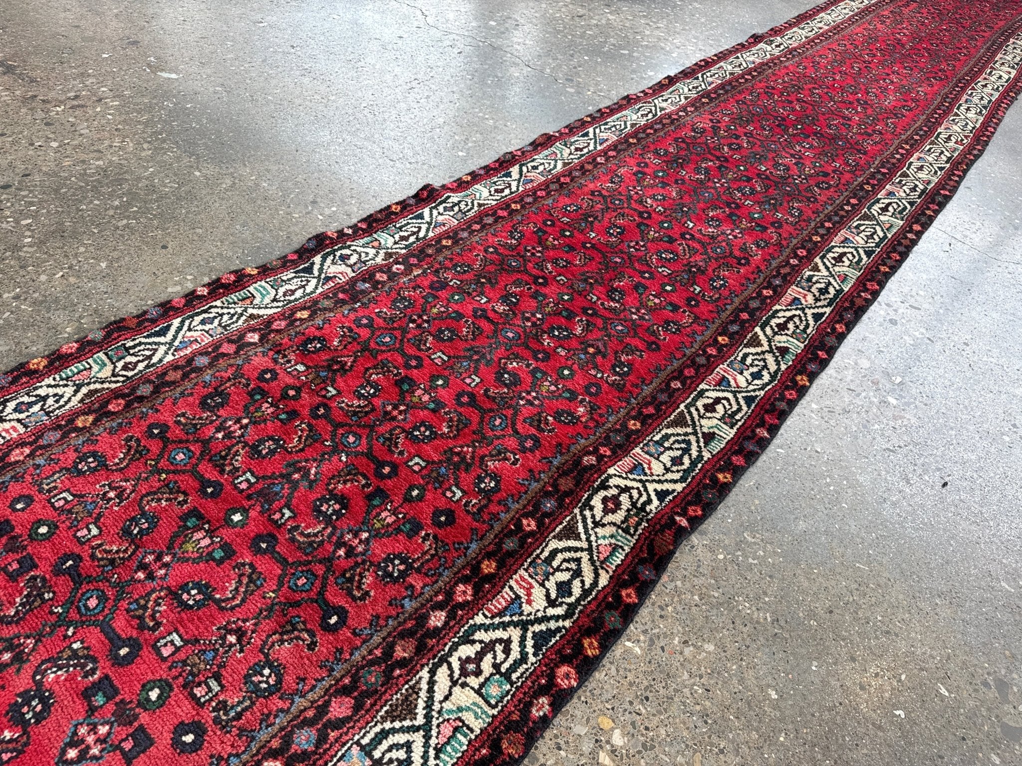 Red runner rug corner view with ornate navy and cream motifs along the edge.