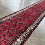 Red runner rug corner view with ornate navy and cream motifs along the edge.