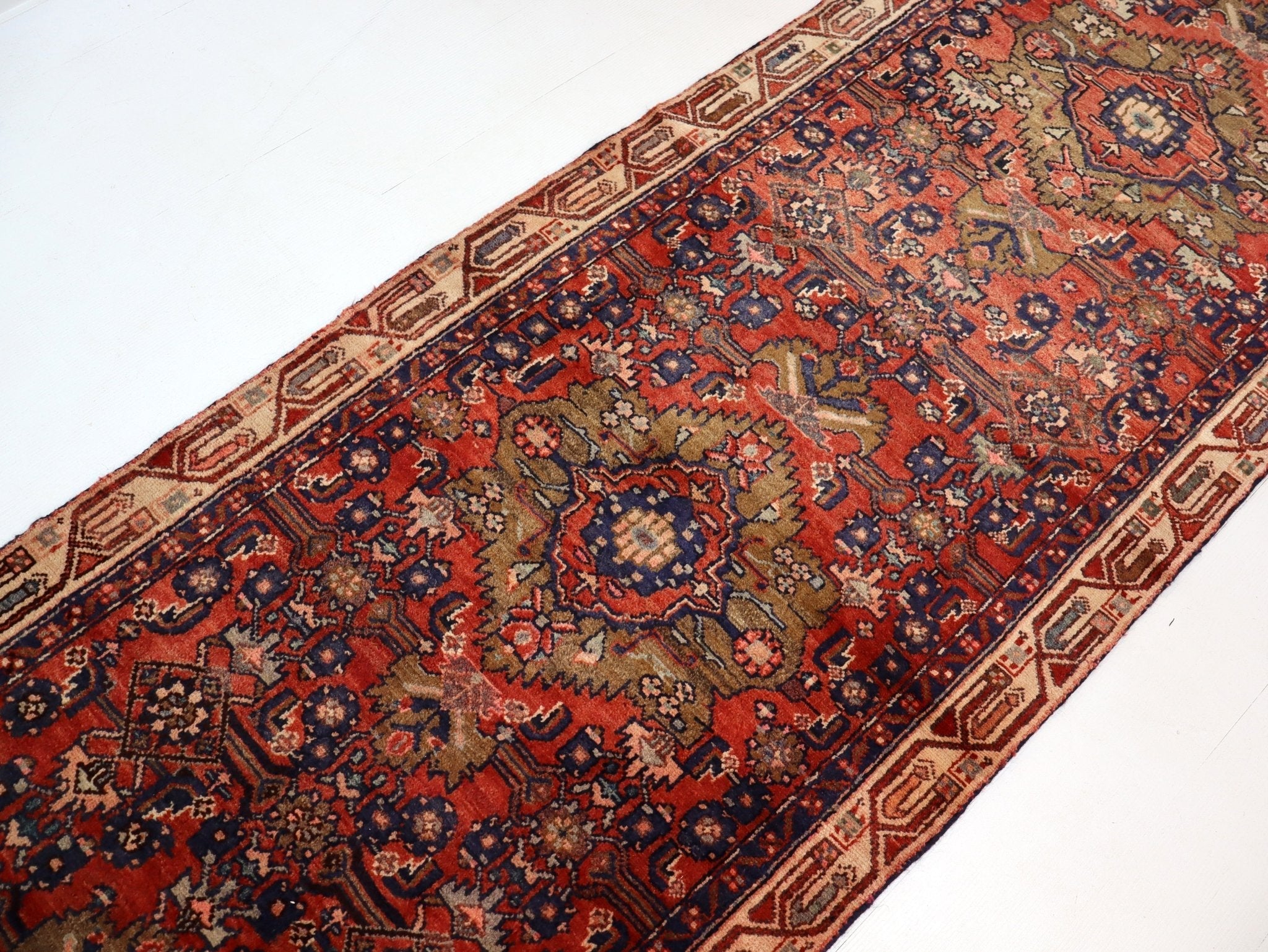 Persian runner rug with red and navy field and beige border, angled view