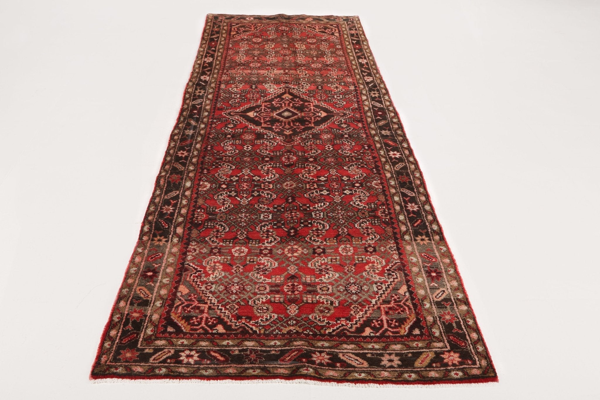 Persian runner rug with red center medallion and repeating motifs, wide border
