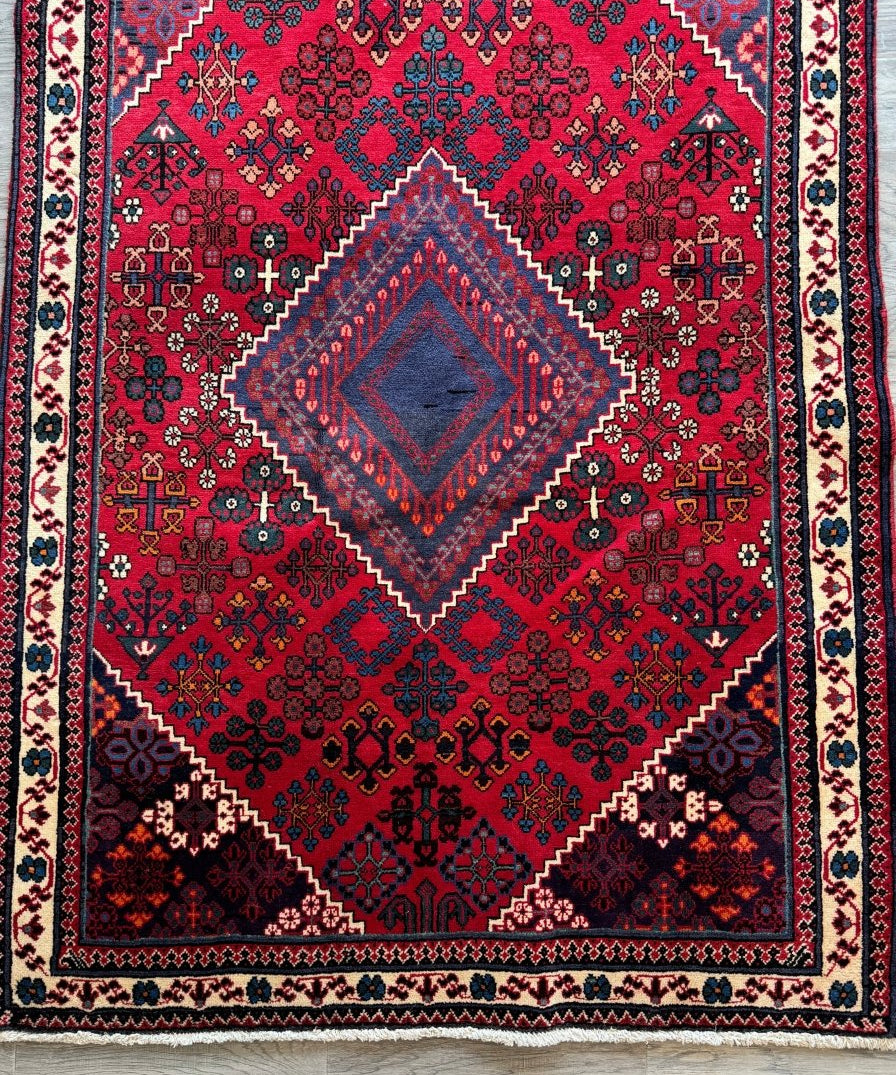 Persian Joshaqan rug with red center medallion and blue accents, full view on floor