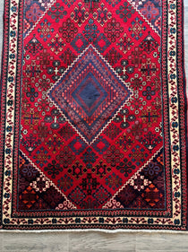 Persian Joshaqan rug with red center medallion and blue accents, full view on floor