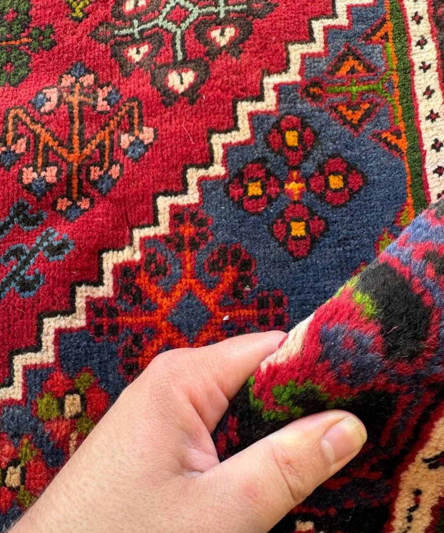 Corner detail of red joshagan rug with navy, green, and cream geometric patterns