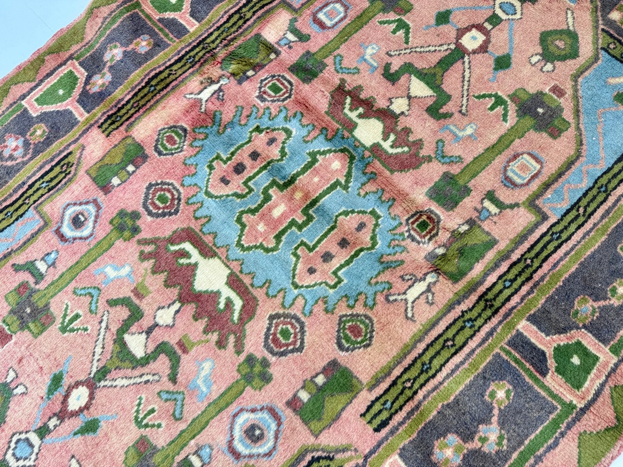 Persian Jozan rug close-up with pink field, green and light-blue motifs, and striped border