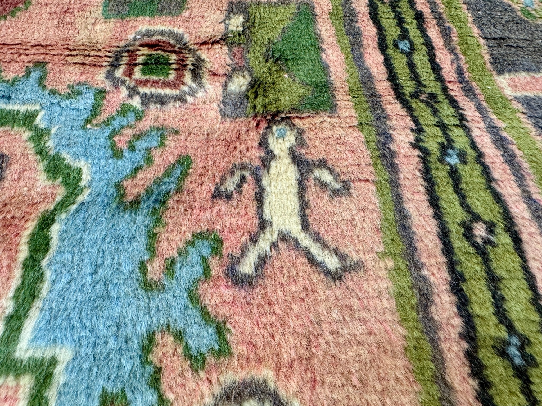 Close-up of Persian rug pile with pink ground, blue shapes, and green accents