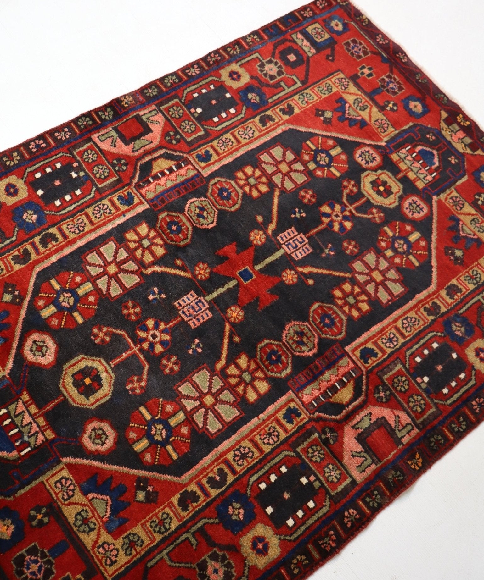 Hamadan rug diagonal view with red border band, navy field, colorful geometric icons