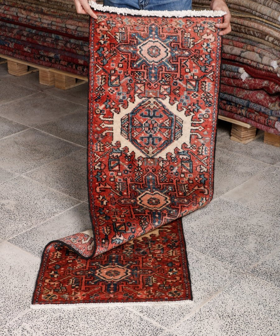 Persian-style runner rug shown folded on tile; terracotta, navy, and cream