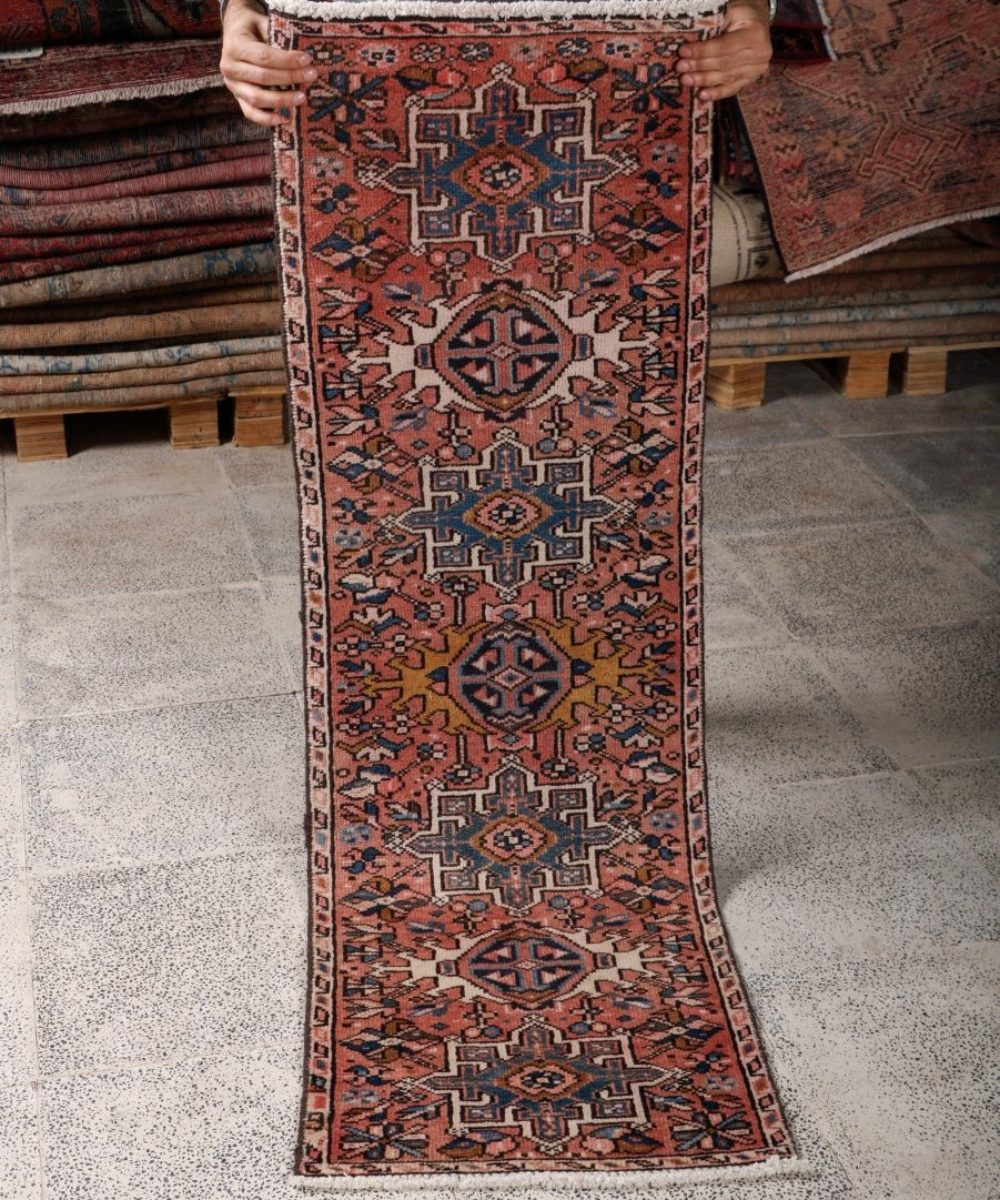 Handheld view of terracotta Persian runner rug with repeating blue diamond motifs