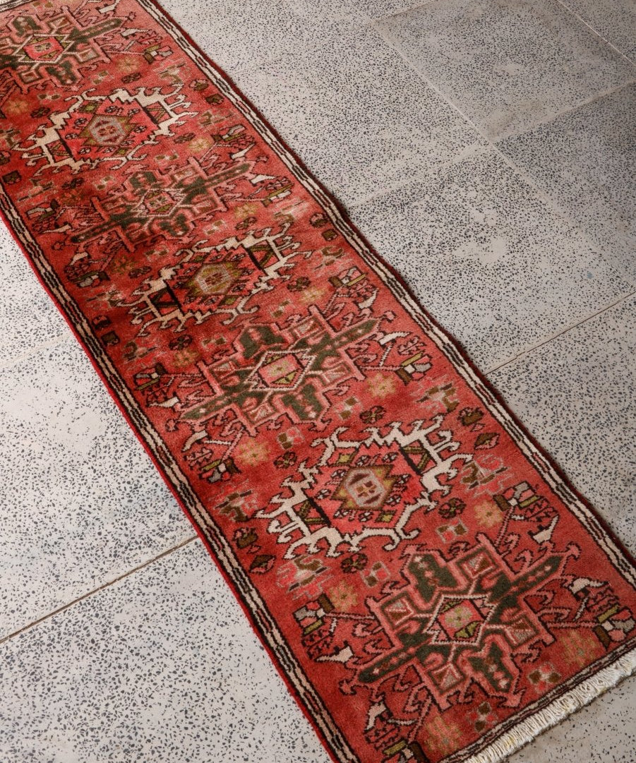 Persian Karaja runner rug angled view, red field with dark border stripe and geometric pattern