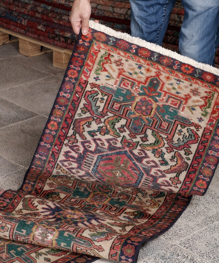 Persian runner rug being laid down; multicolor geometric pattern with red and teal border