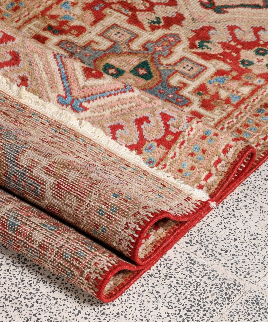 Corner of red Persian-style runner rug with fringed ends and multicolor geometric design