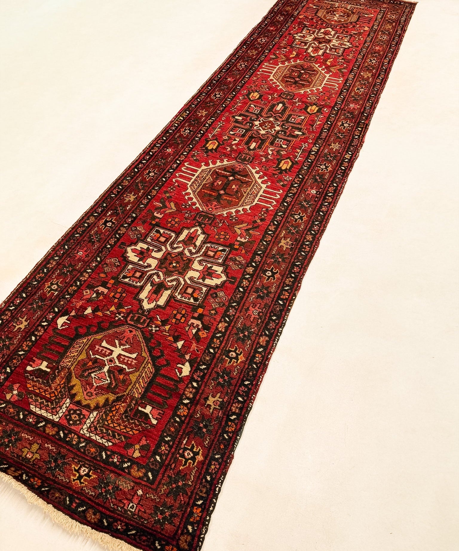 Red runner rug with geometric panel design, dark border, and short fringe