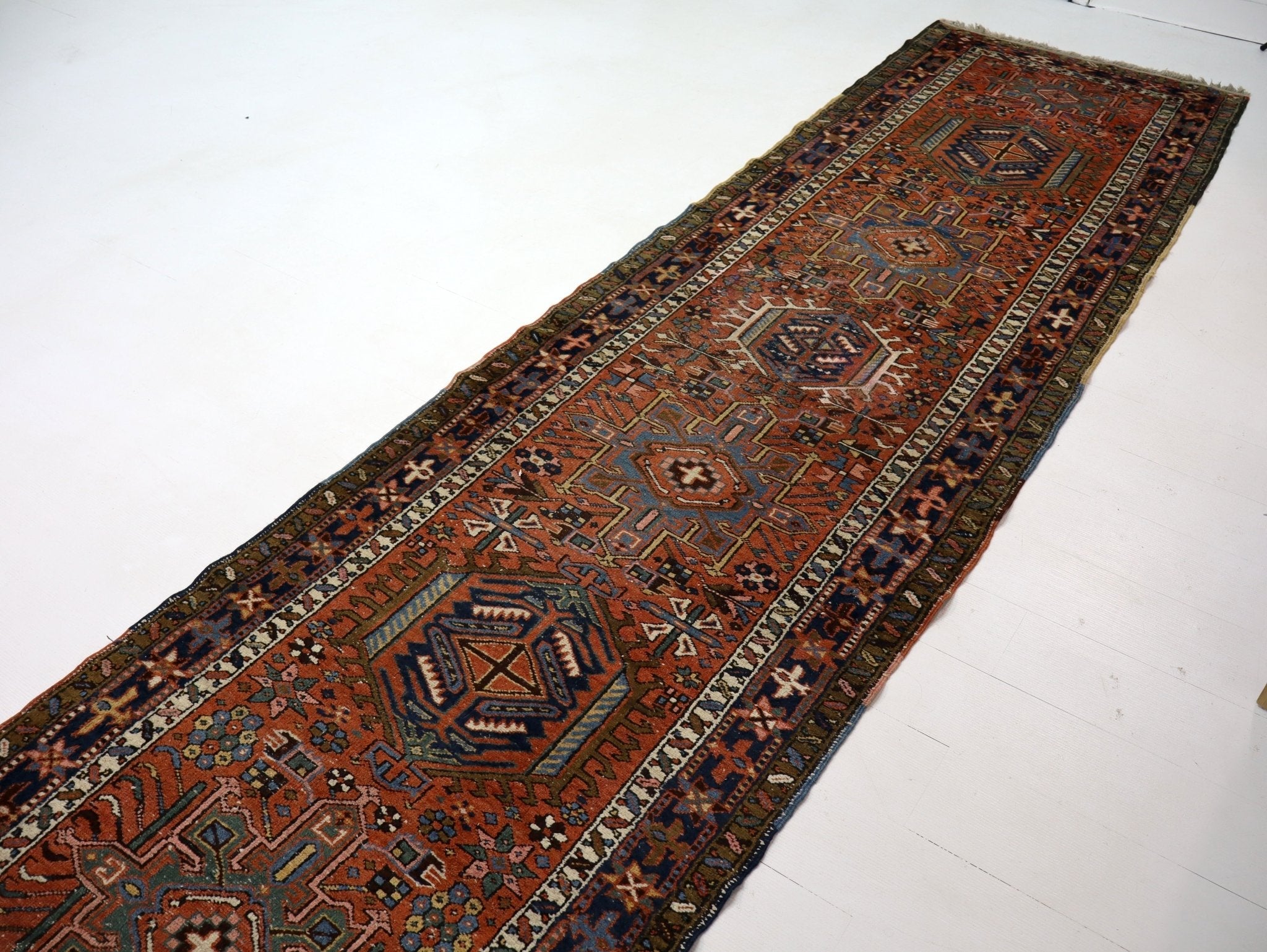 Runner rug angled on white floor with rust and navy medallions and border trim.