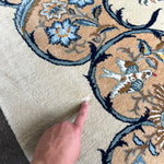Persian Kashan rug with blue-outlined floral motif on cream ground, finger pointing