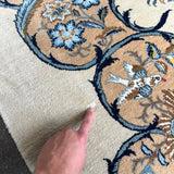 Persian Kashan rug with blue-outlined floral motif on cream ground, finger pointing