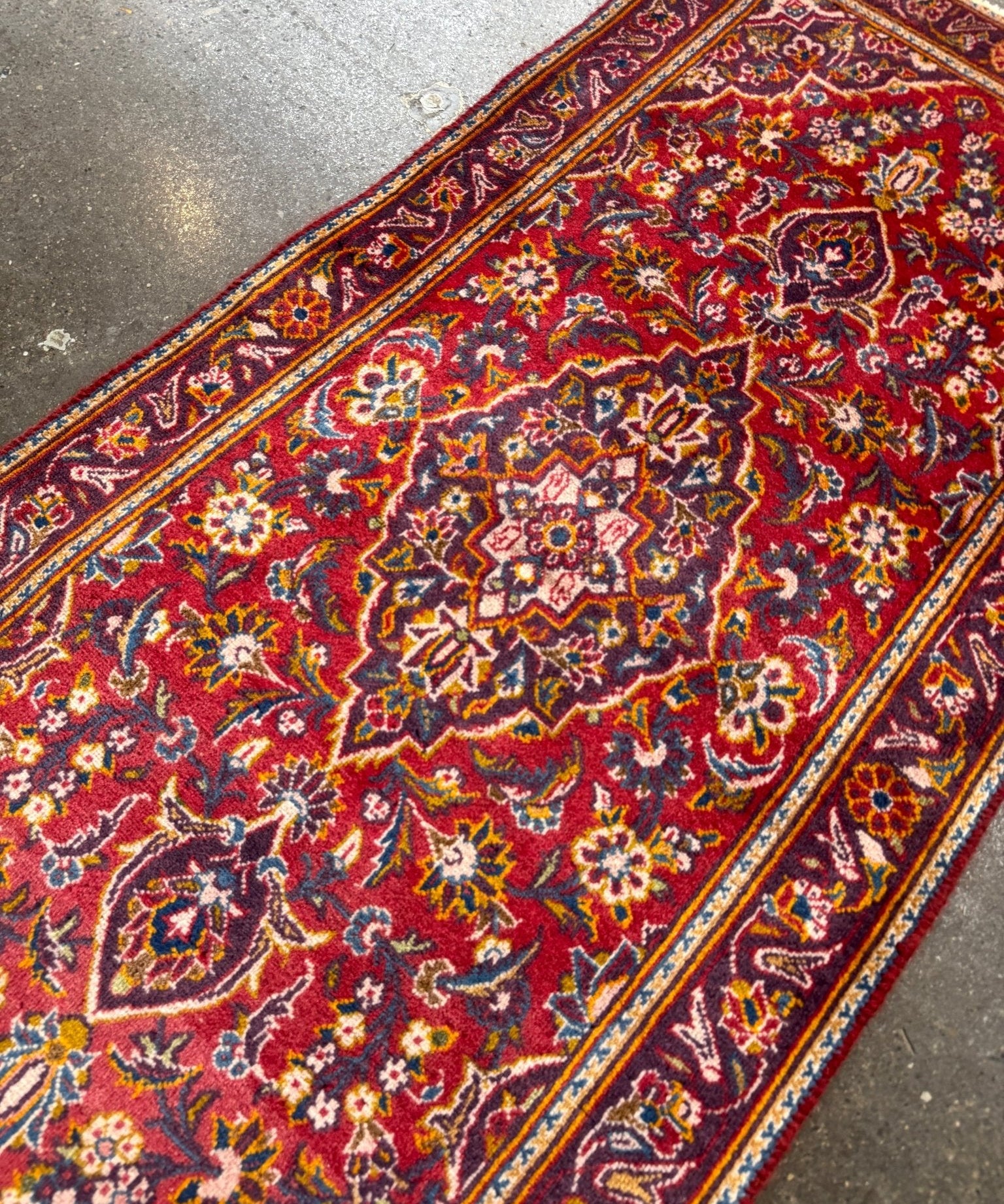 Kashan rug angled view with red field, ornate floral center and multicolor border