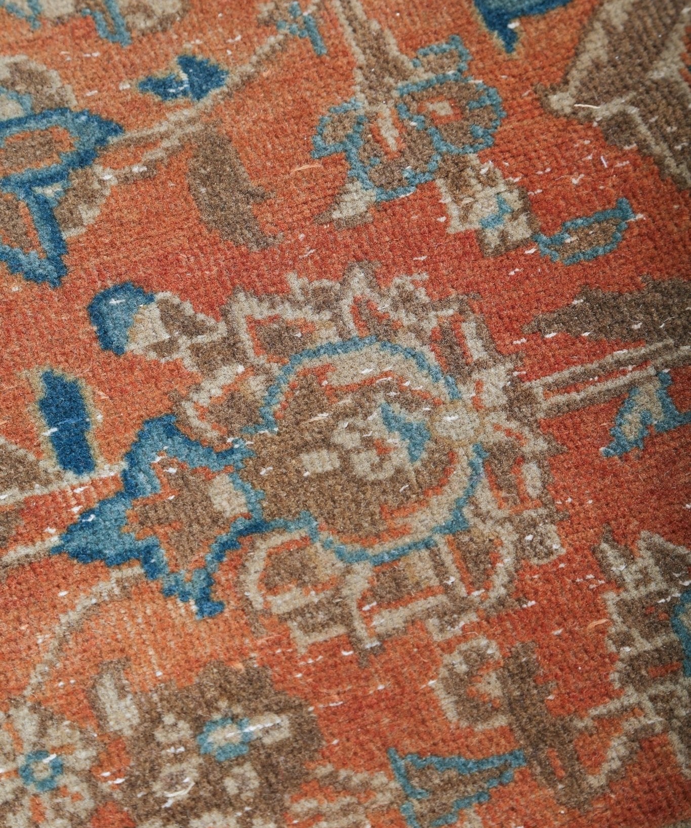 Orange rug close-up with blue floral motifs and distressed gray patterning