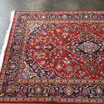 Red Persian-style area rug with central medallion, ornate navy border, and fringe