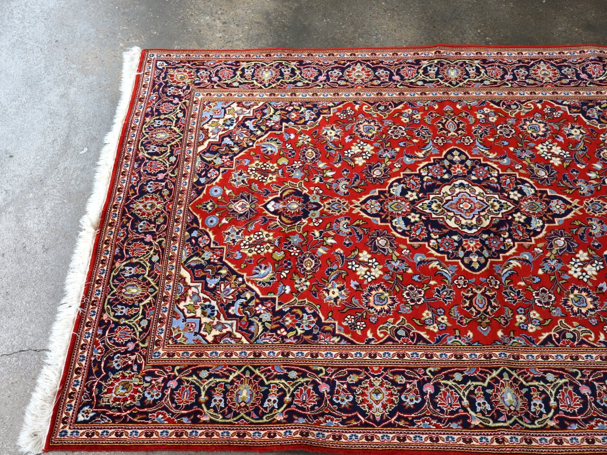 Red Persian-style area rug with central medallion, ornate navy border, and fringe