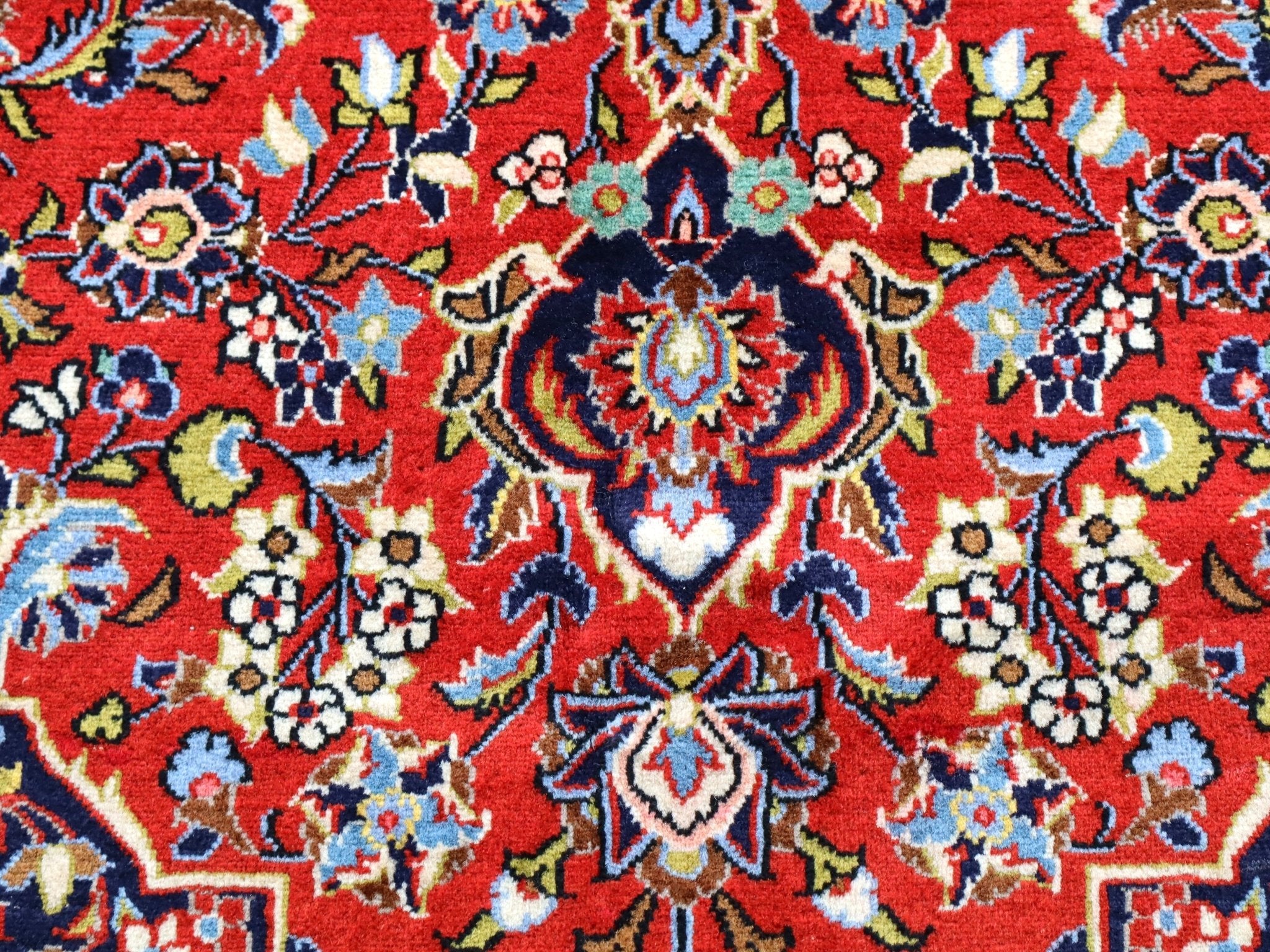 Close-up of rug medallion with red backdrop, blue accents, and cream floral highlights