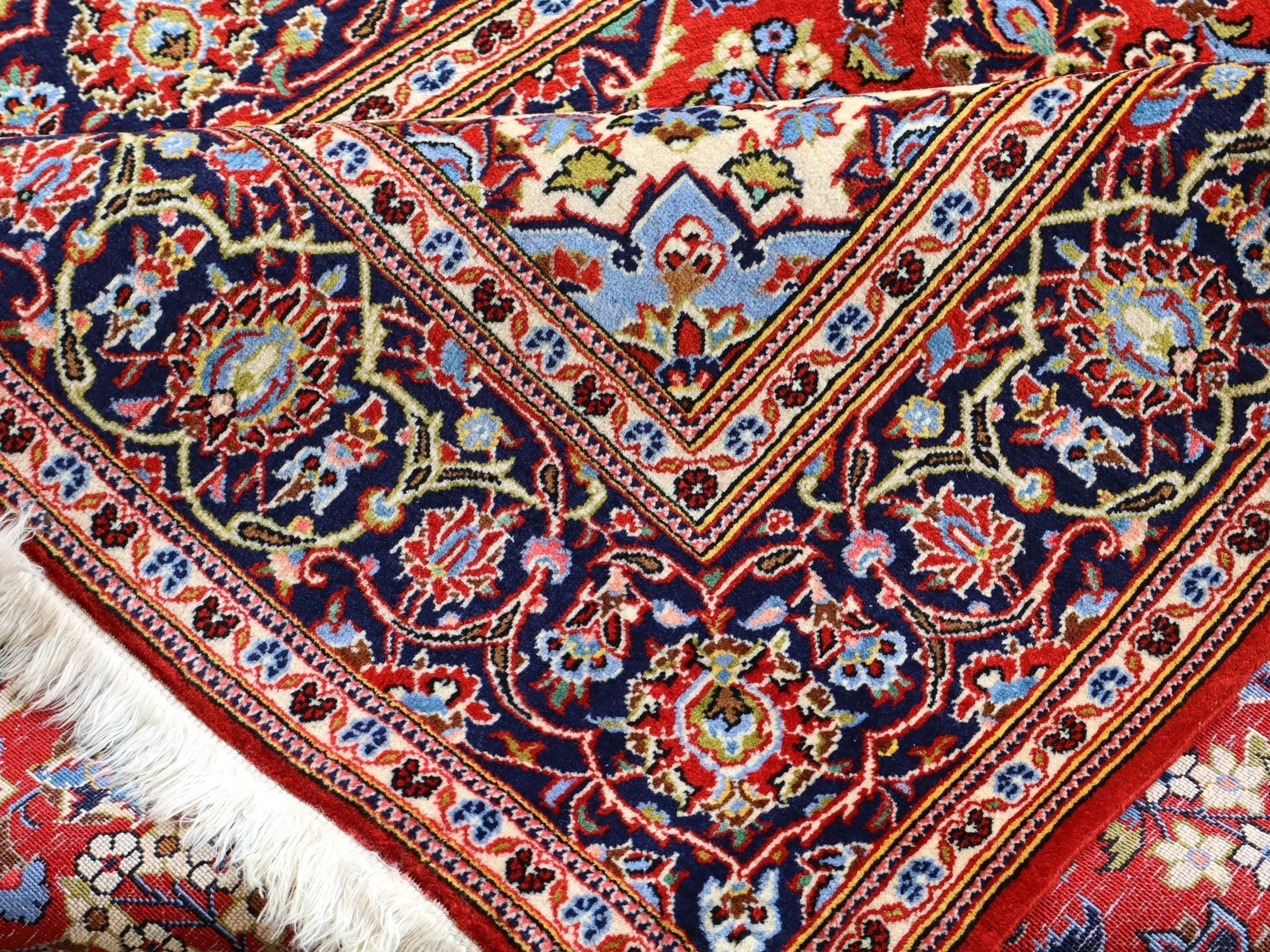 Persian Kashan rug close-up corner: red and navy pattern with cream accents, short fringe
