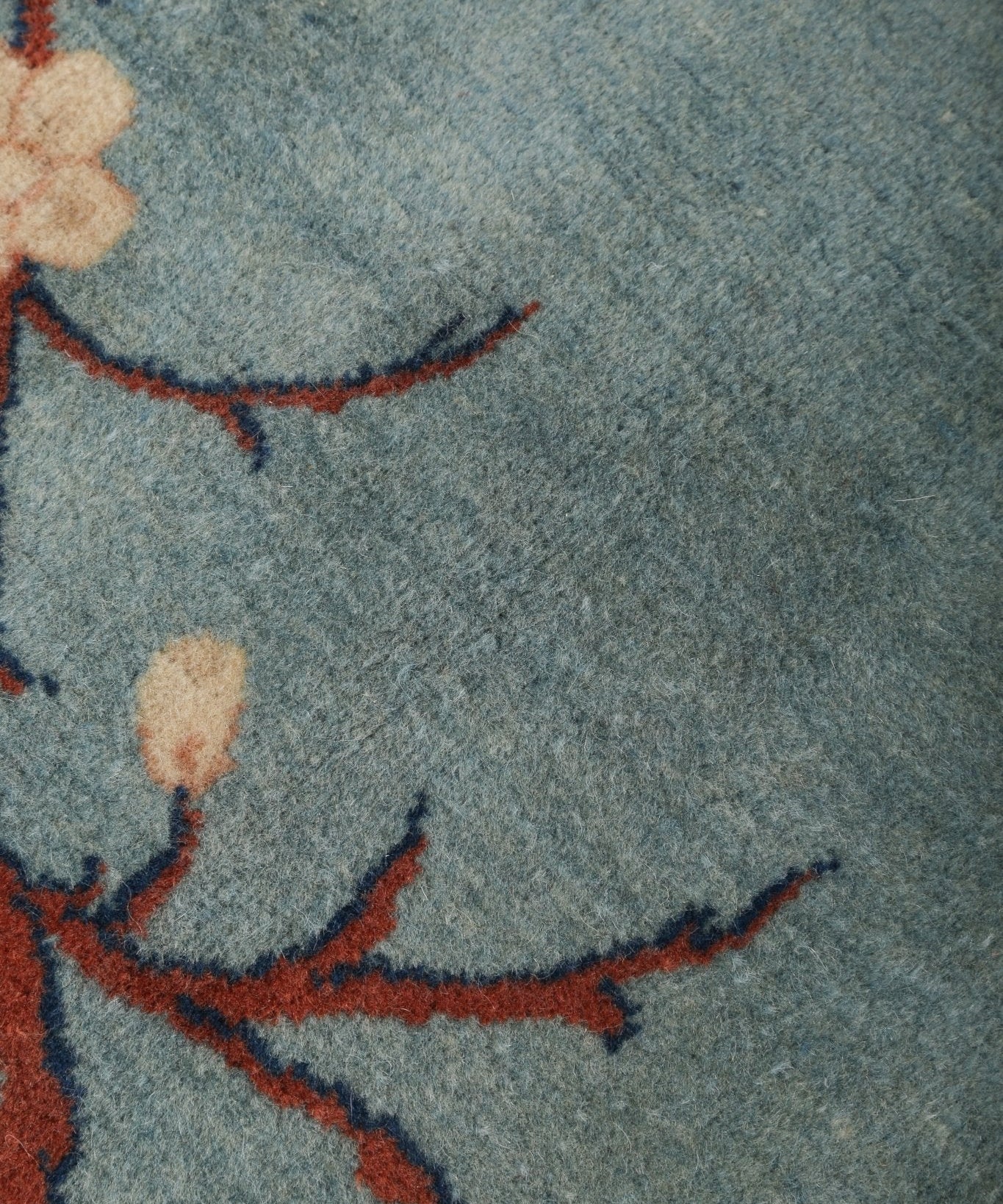 Tight crop of light blue rug with cream flower touches and red-orange vine lines